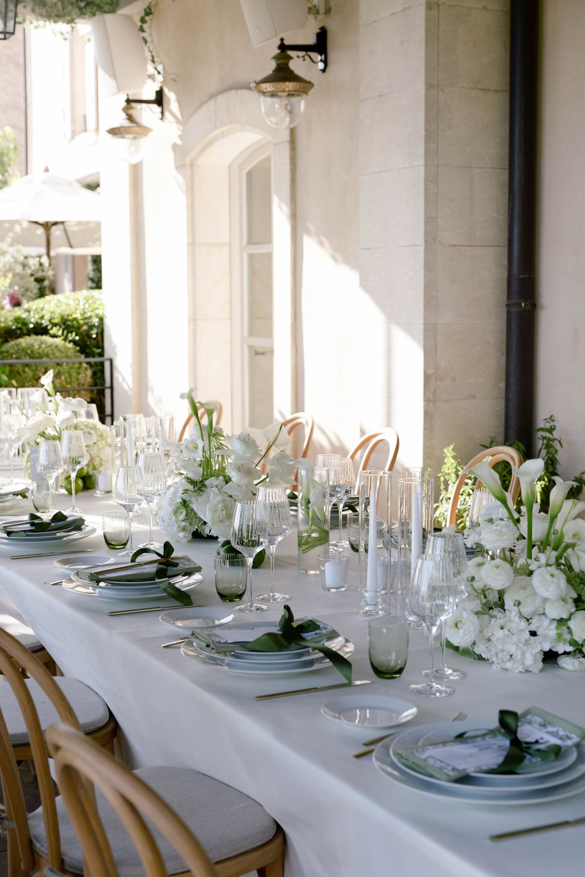 Dinner table with calla lilies and green glassware under a vine pergola