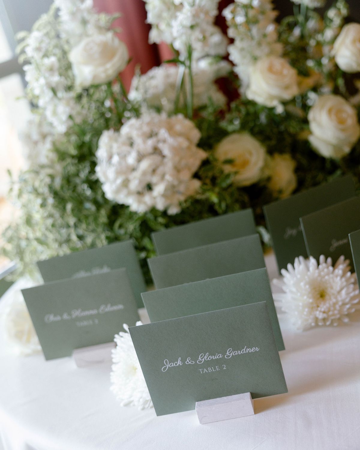 Green escort cards with white calligraphy among white flowers
