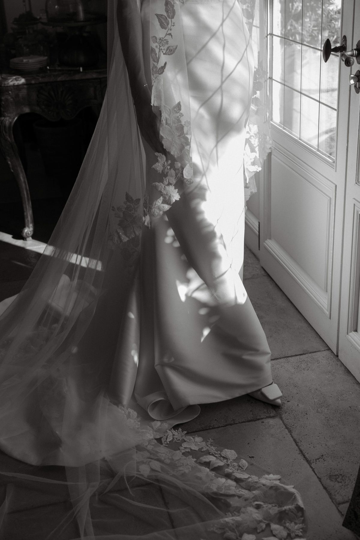 Black and white photo of the bride’s gown and lace veil by a glazed door