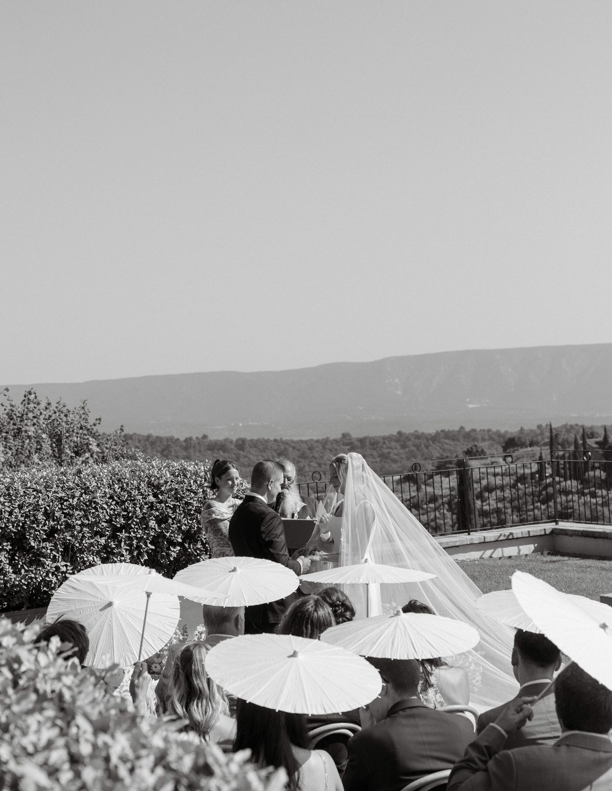 Black and white photo of the ceremony beyond a row of parasols