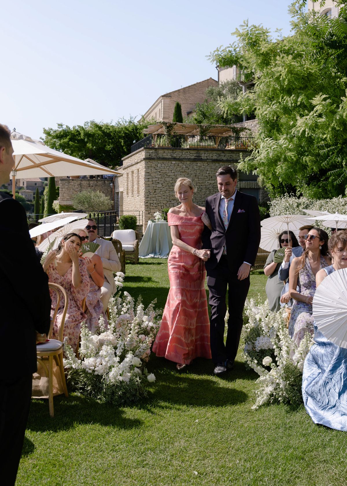 Guest in a coral gown escorted down the aisle by a man in a dark suit