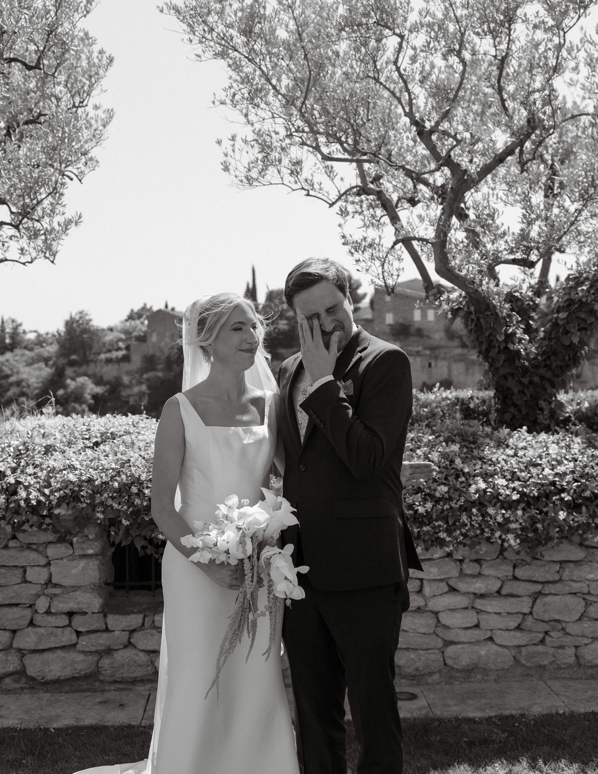Black and white photo of the bride beside a tearful man in a dark suit in the garden