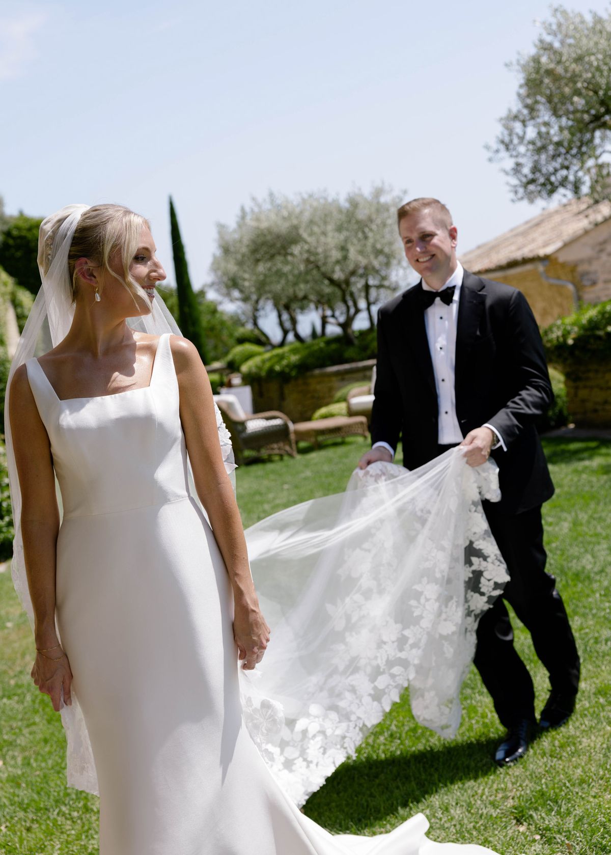 Groom carrying the bride's veil across the lawn