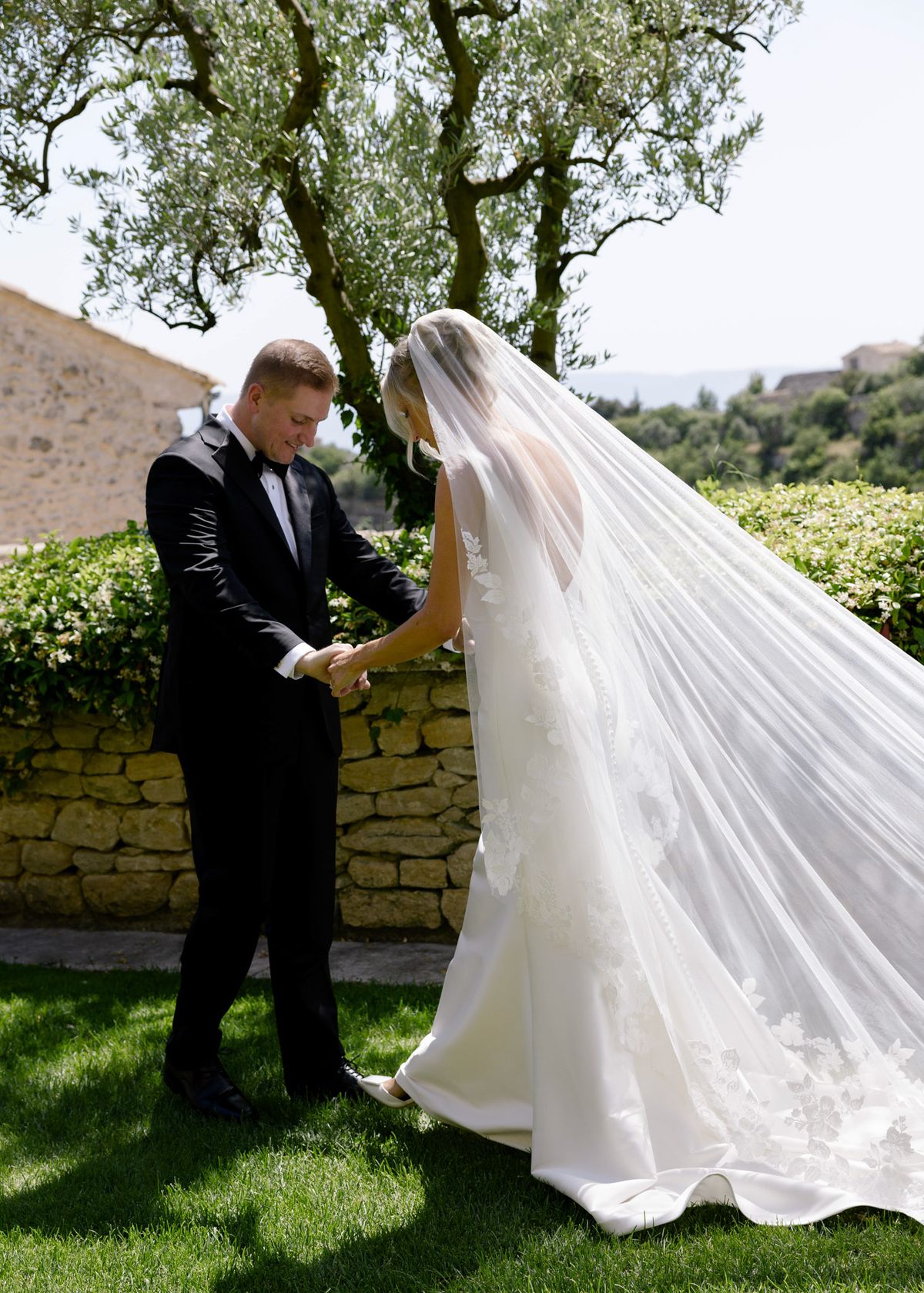 Groom holding the bride’s hands beneath an olive tree at the first look