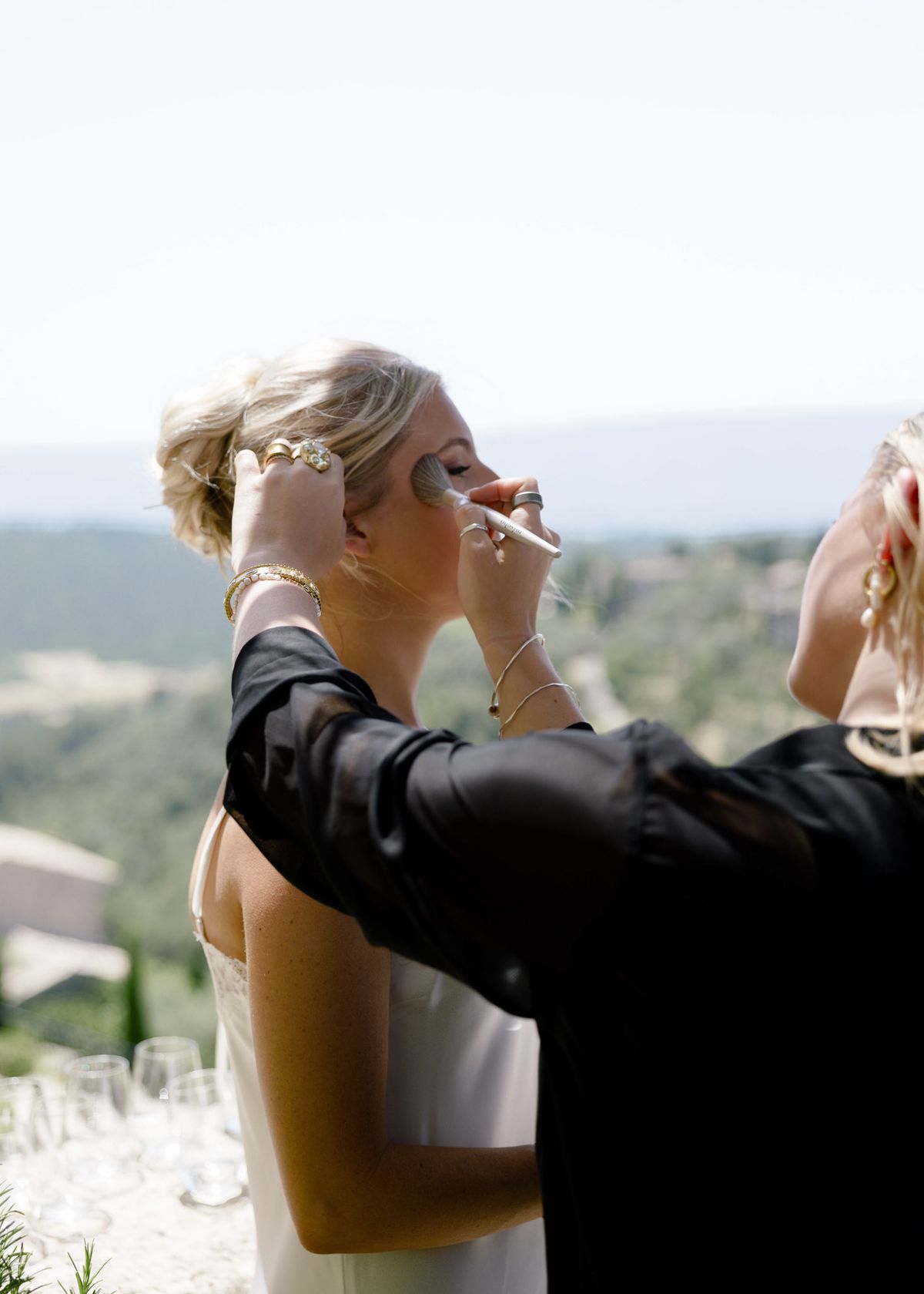 Make-up artist finishing the bride’s make-up on a terrace above the valley