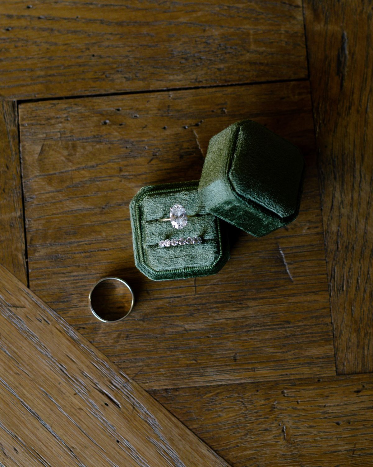 Engagement ring in a green velvet box beside a wedding band