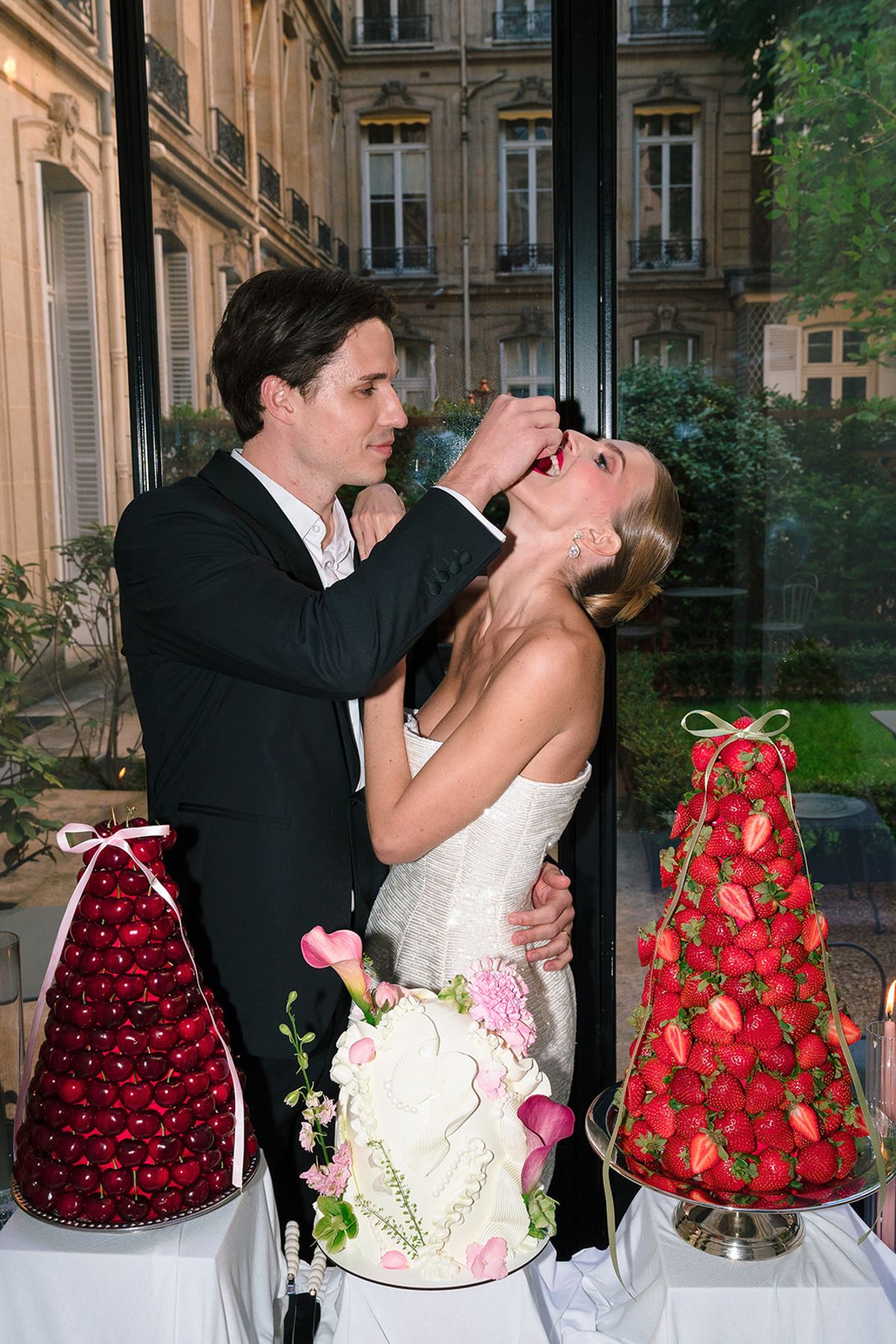 Groom feeding the bride a strawberry beside the cake and fruit towers