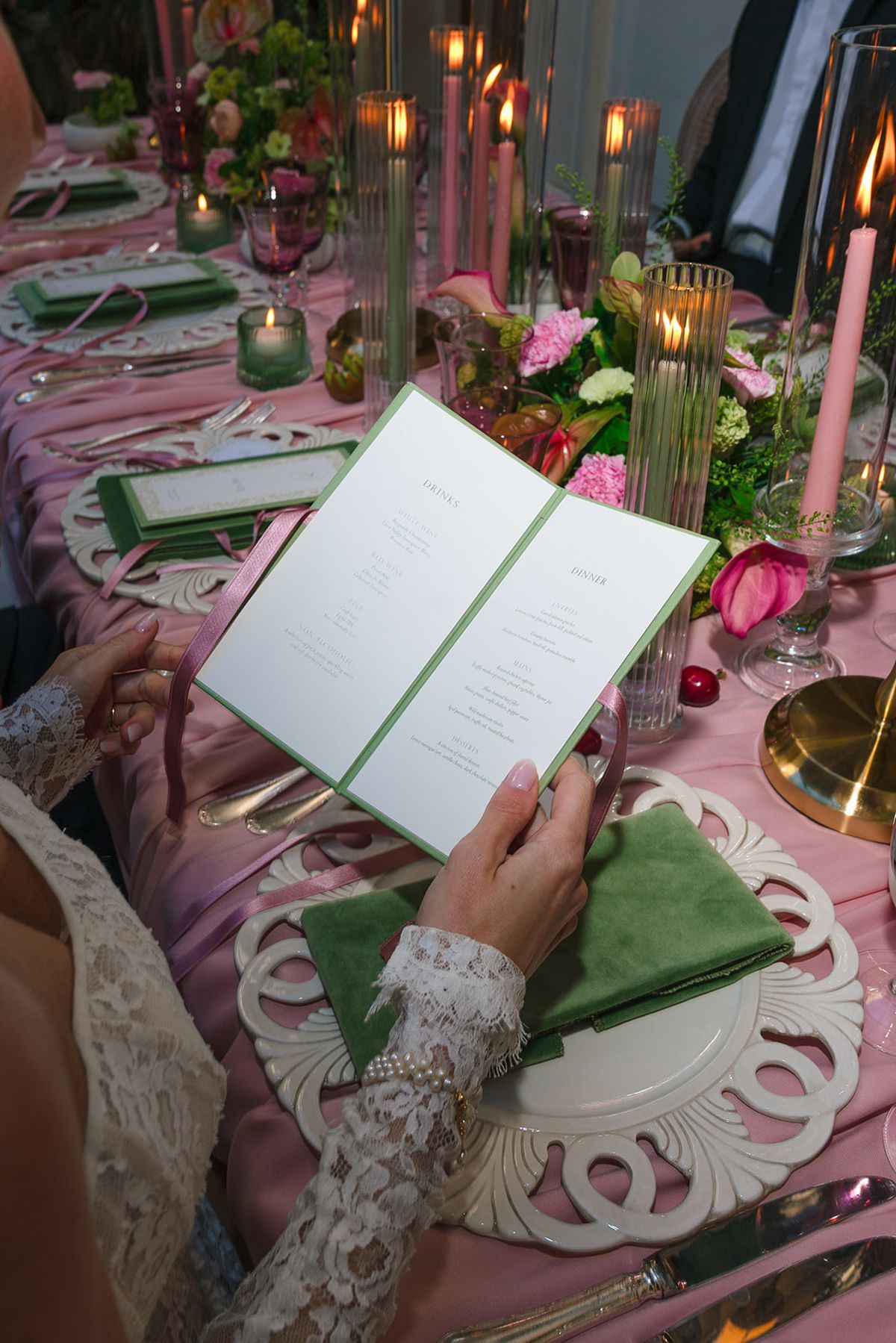 Guest reading a green menu at the candlelit pink dinner table