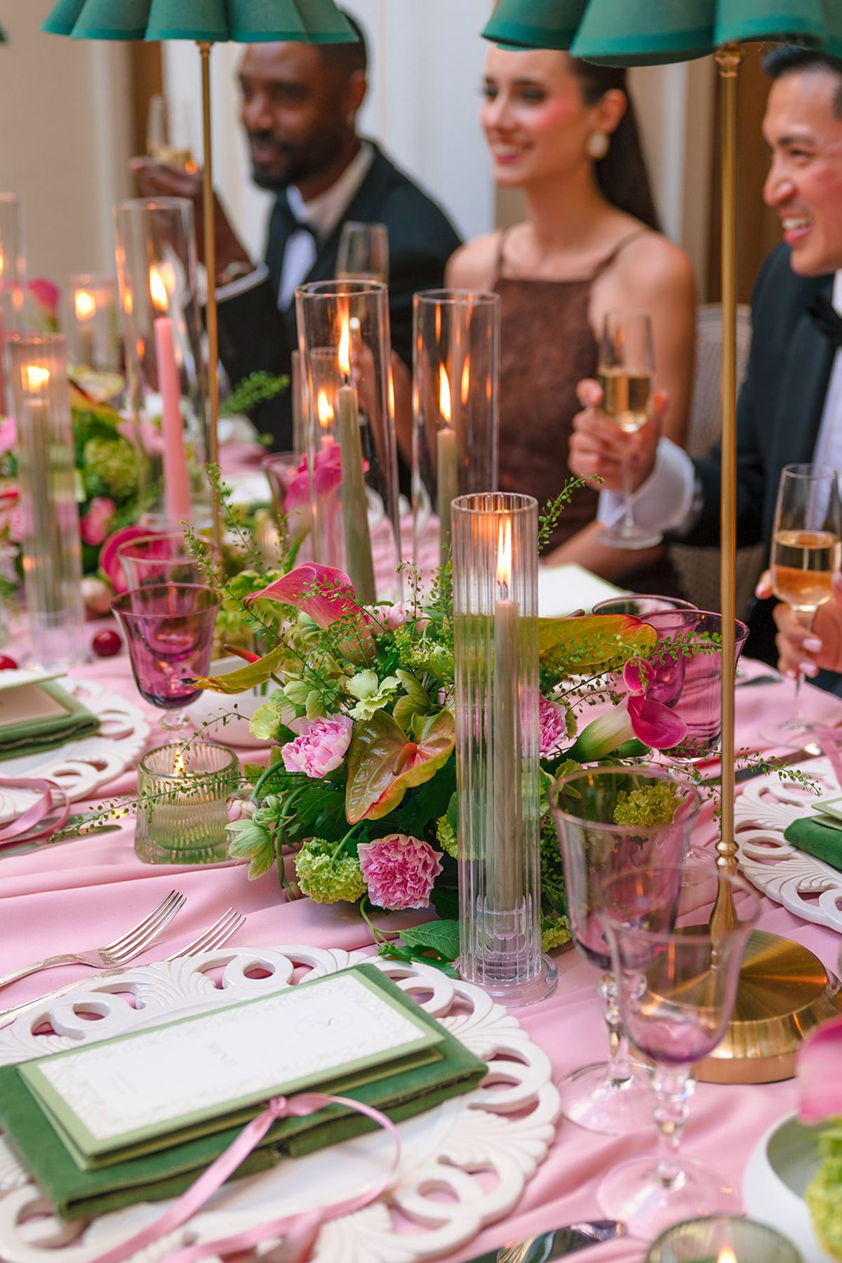 Guests at the candlelit dinner table with pink and green florals and champagne