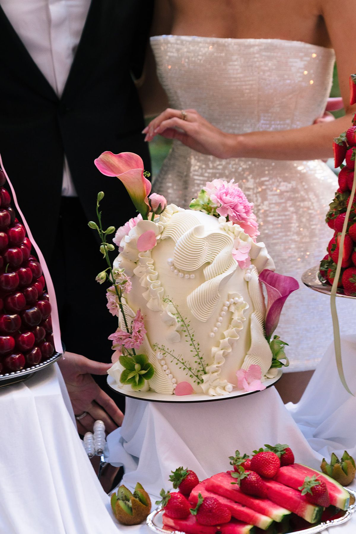 Sculpted white wedding cake with pink calla lilies beside the bride's beaded gown