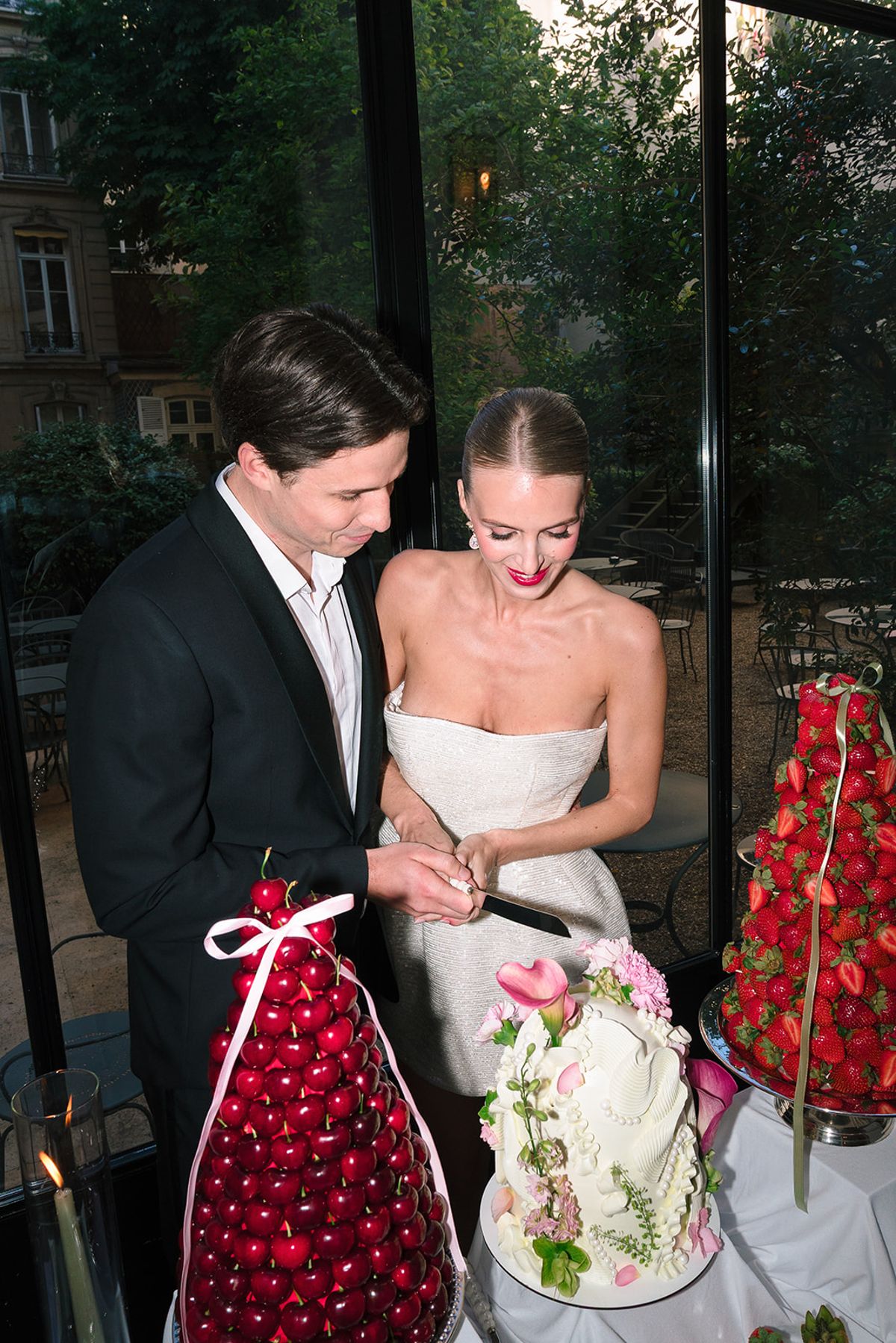 Bride and groom cutting a sculpted white wedding cake beside strawberry and cherry towers