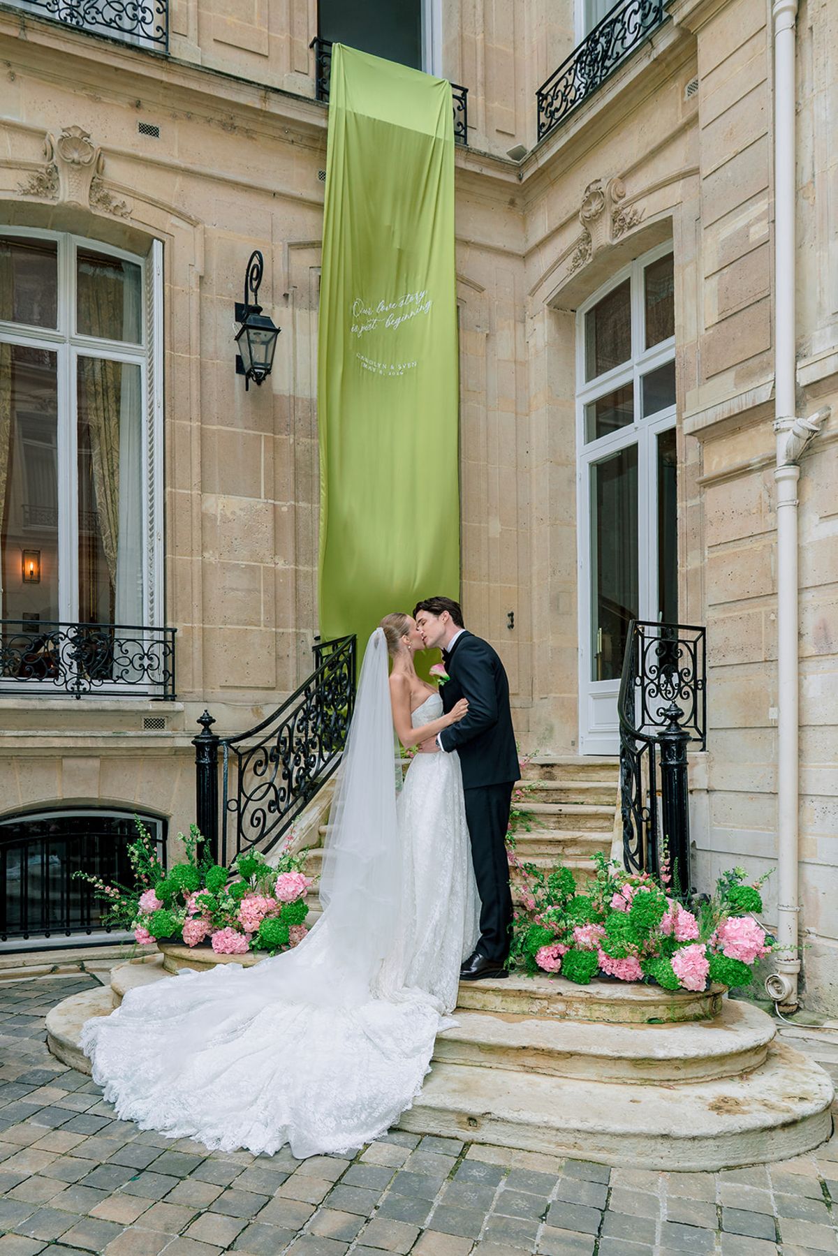 Bride and groom kissing beneath a green banner on the courtyard steps at Hôtel Alfred Sommier