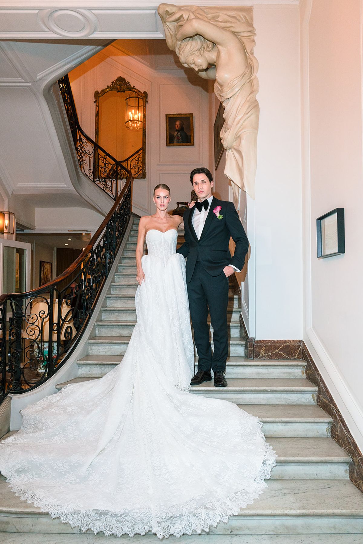 Bride and groom standing on the grand staircase with her train spread across the steps, Hôtel Alfred Sommier