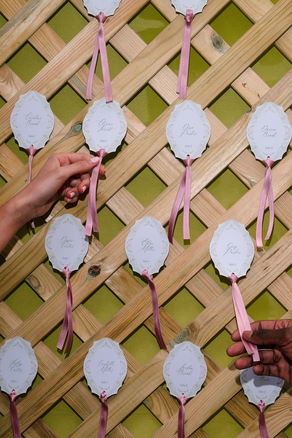 Scalloped escort cards tied with pink ribbon on a wooden trellis