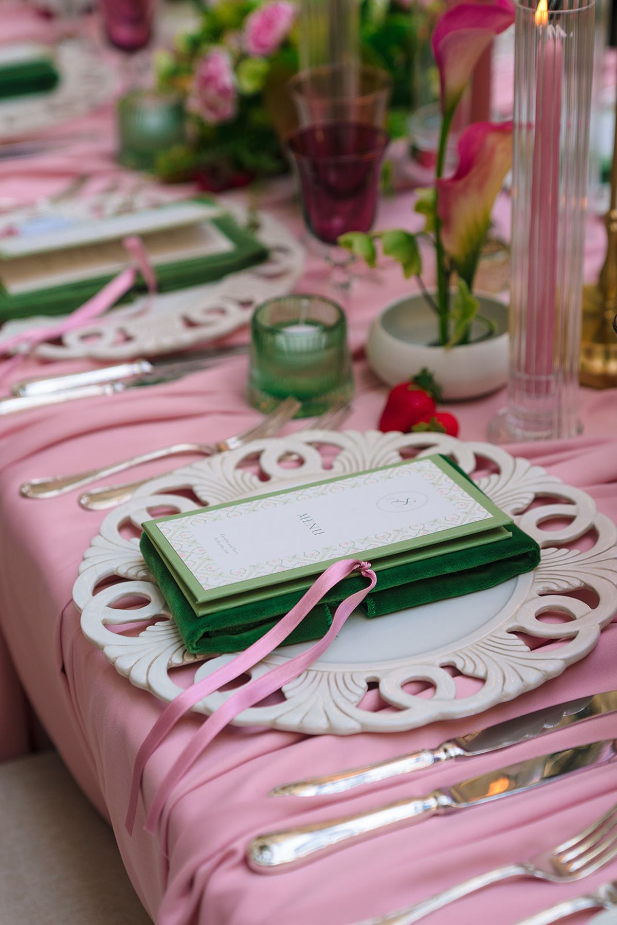 Place setting with green velvet menu tied in pink ribbon on a pink tablecloth