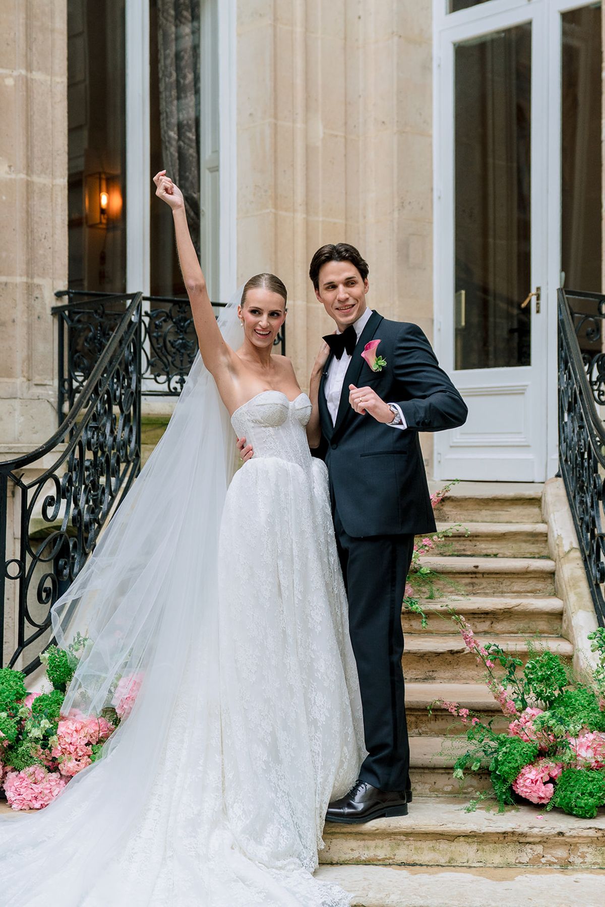Bride raising her arm in celebration beside the groom on the courtyard steps, Hôtel Alfred Sommier
