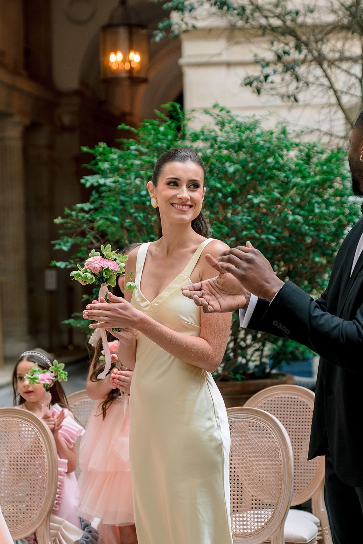 Bridesmaid applauding in the courtyard with flower girls among the guests