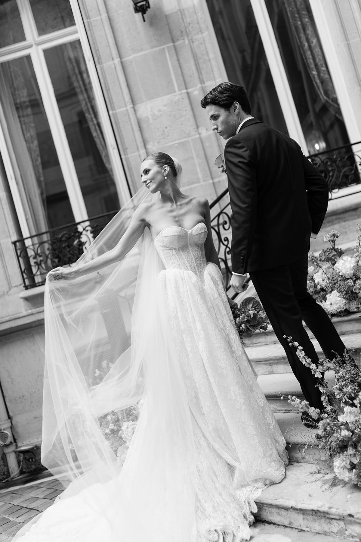 Black and white portrait of the bride lifting her veil as the groom leads her up the courtyard steps