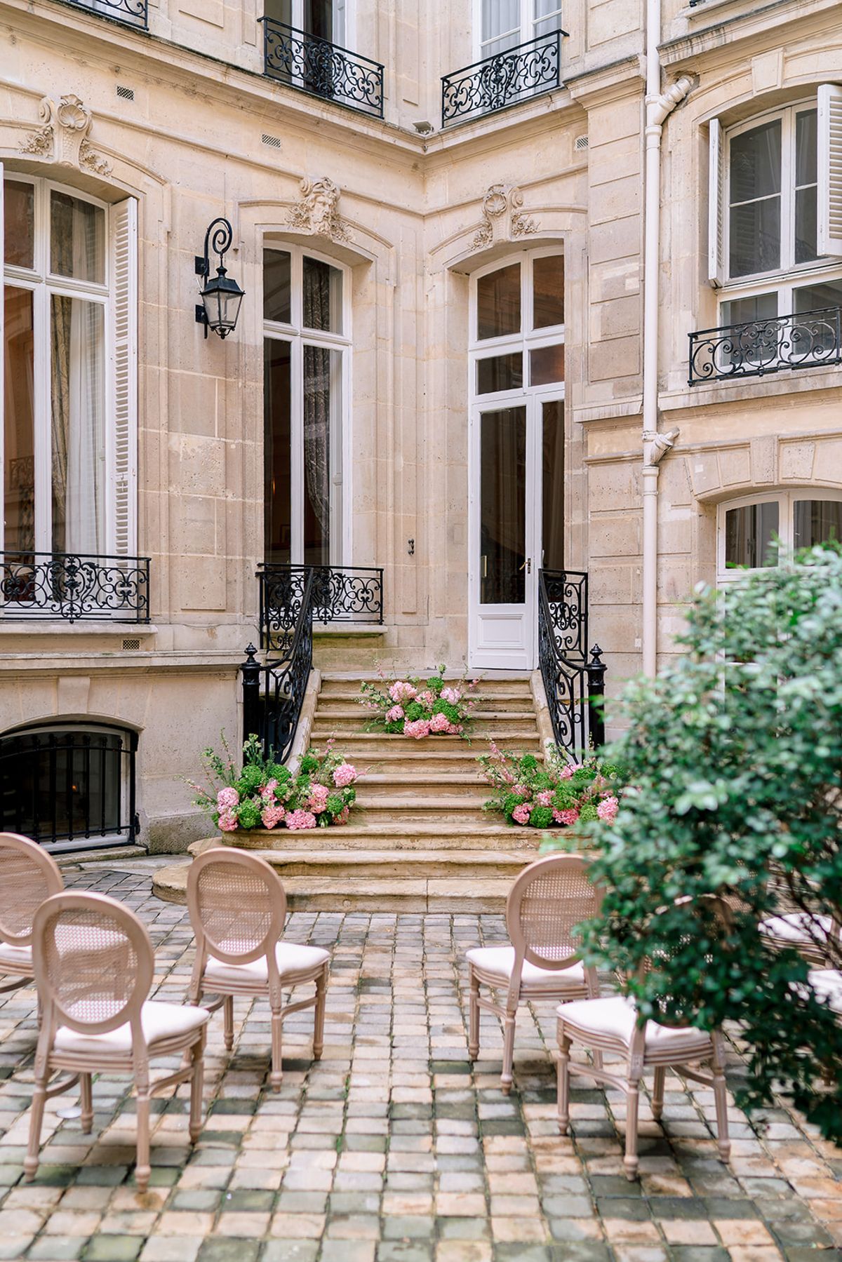 Cobblestone courtyard set with cane chairs and pink hydrangeas before the ceremony, Hôtel Alfred Sommier