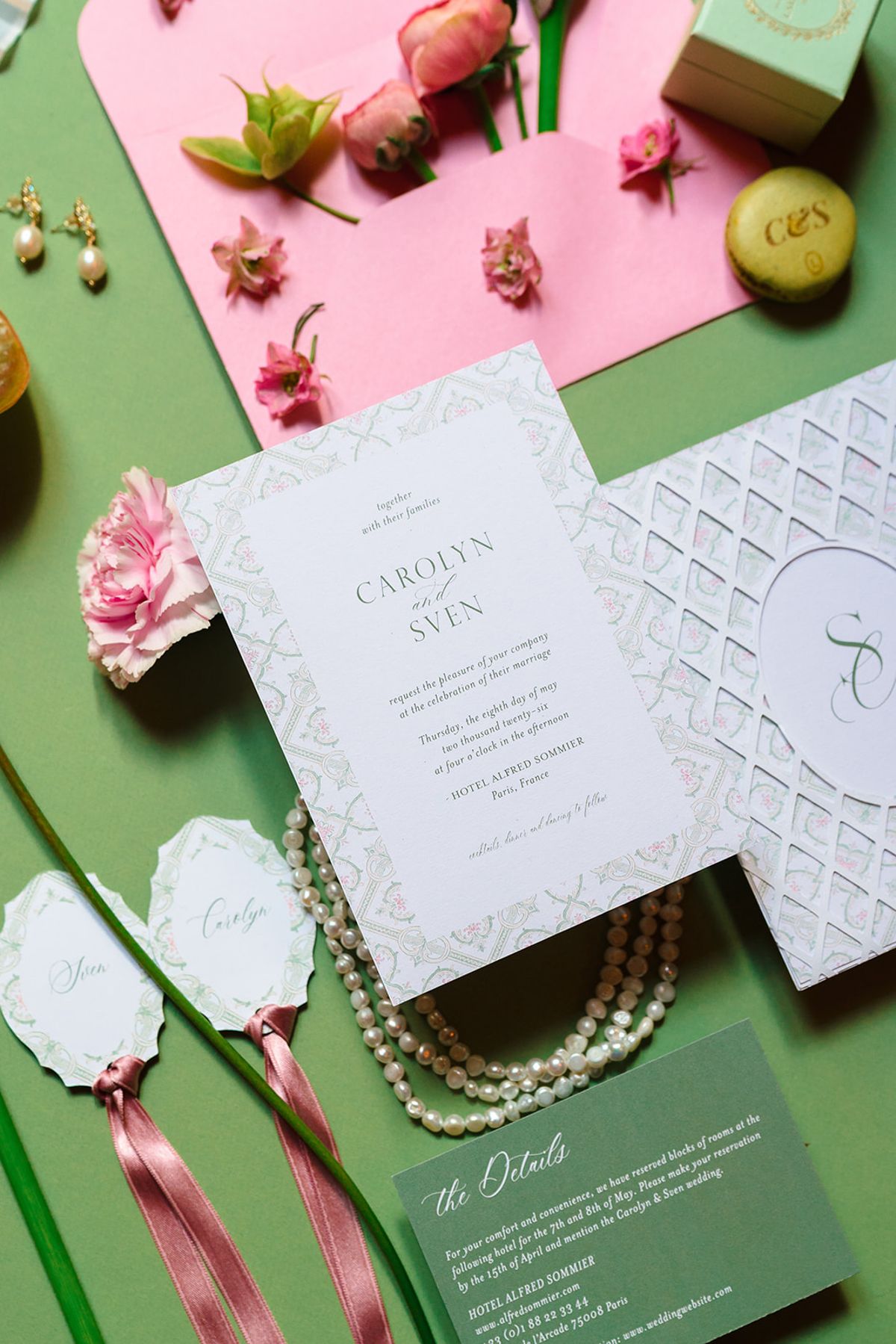 Wedding invitation suite with pink envelope, pearls and ribbon-tied place cards on a green background