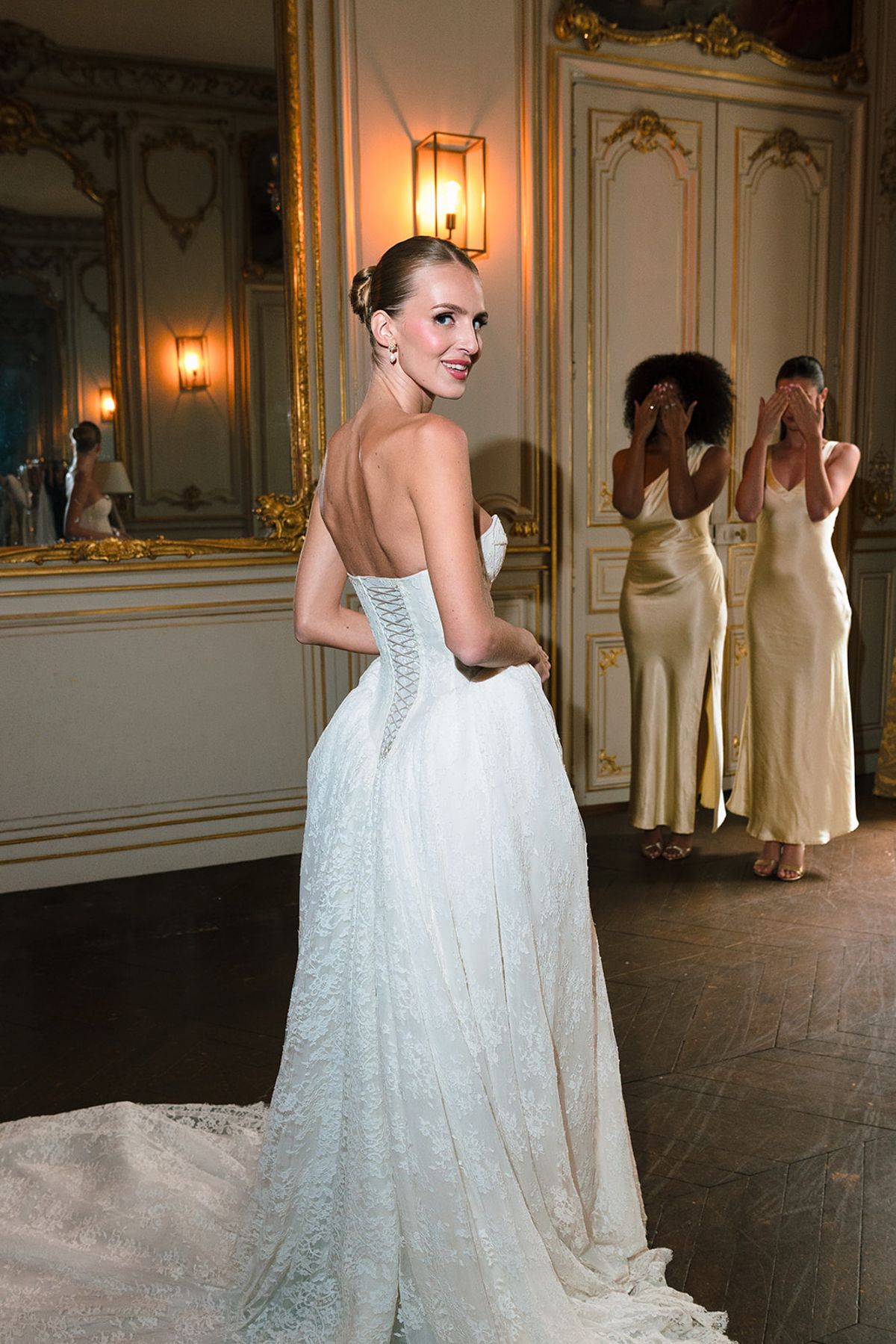 Bride turning to face two bridesmaids in gold satin dresses in a gilded salon at Hôtel Alfred Sommier