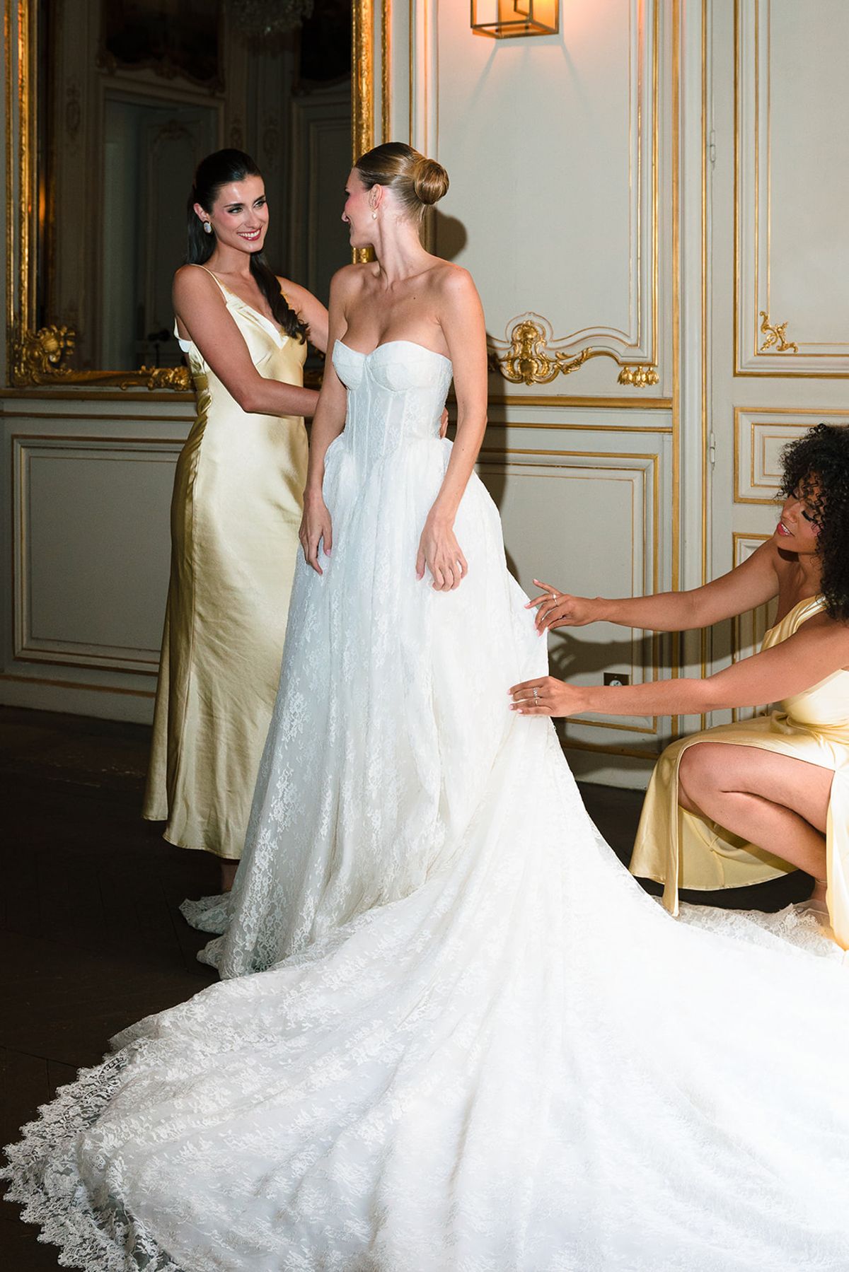 Bridesmaids helping the bride into her gown in a gilded salon at Hôtel Alfred Sommier
