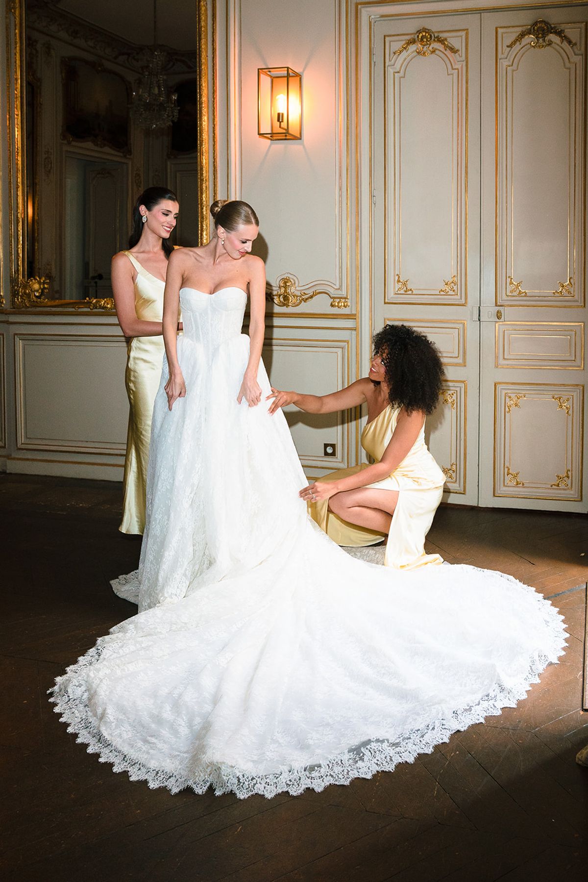 Bridesmaids arranging the bride's lace cathedral train in a gilded salon at Hôtel Alfred Sommier