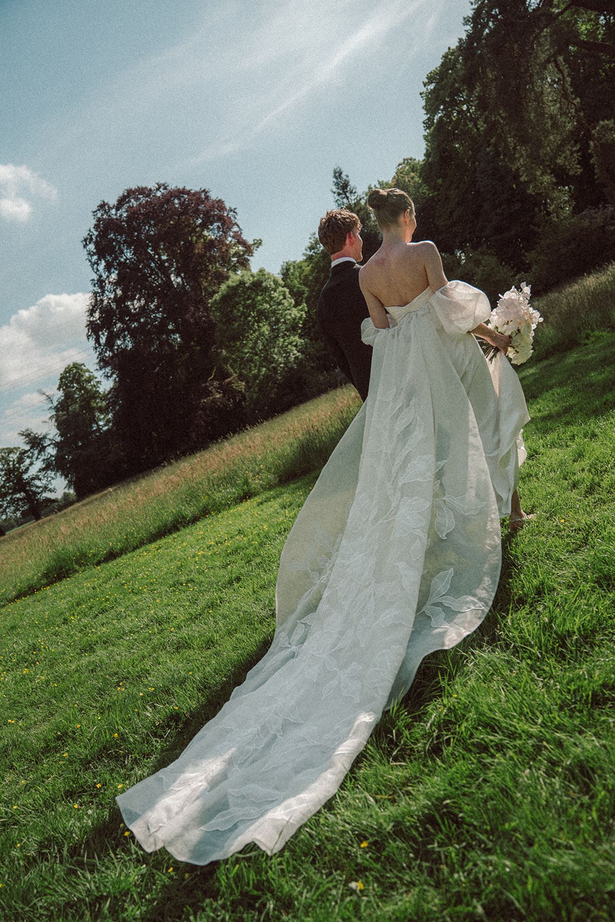 Bride walking across a hillside, her dress trailing behind her