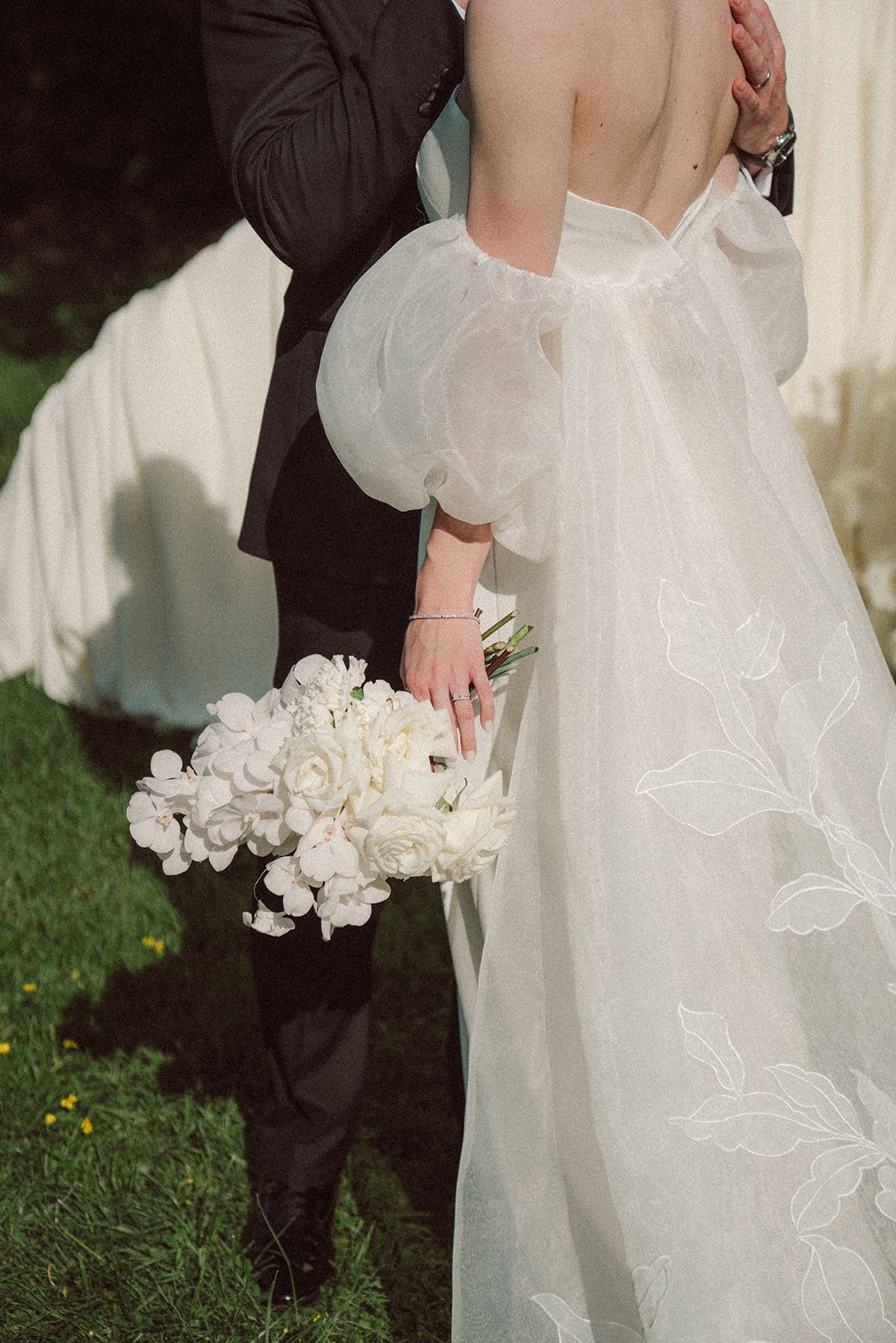 Groom's hand holding the bride's, bouquet between them