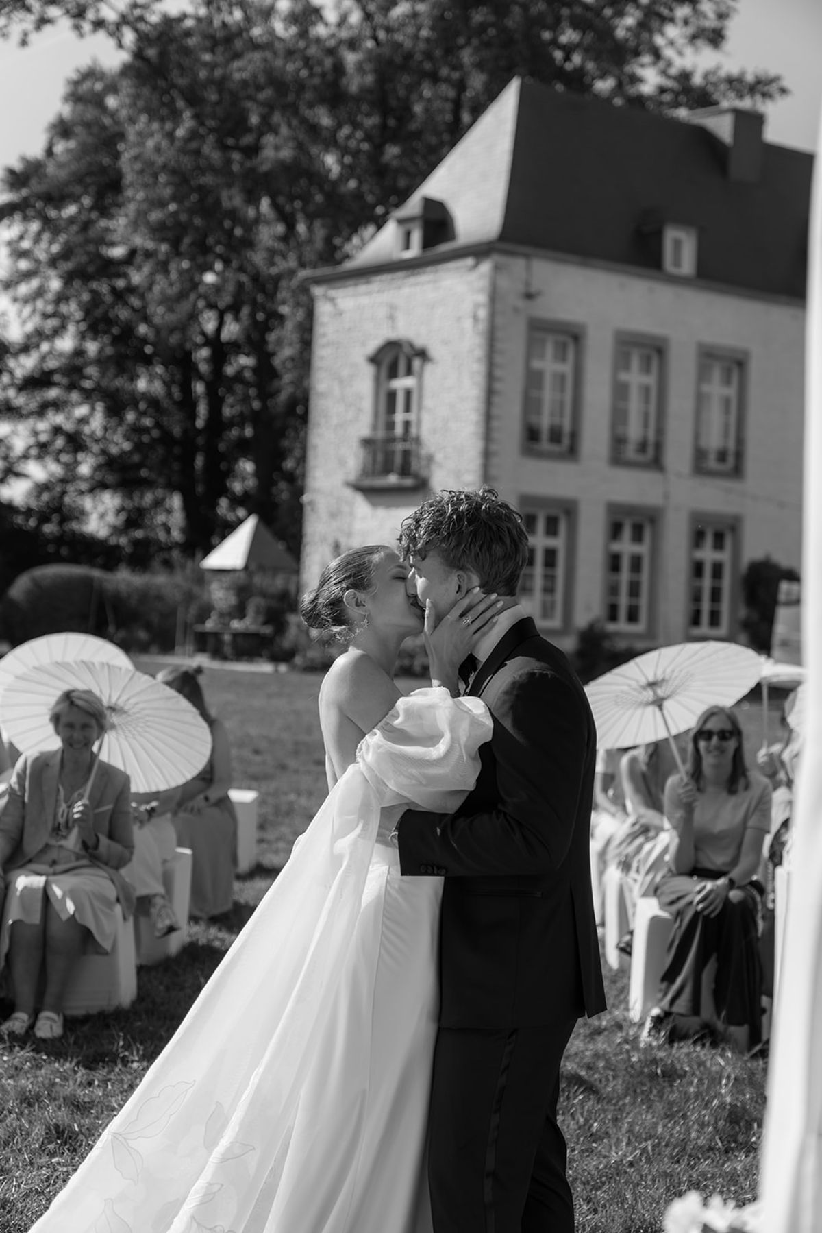 Bride and groom kissing at the ceremony, guests with parasols on either side