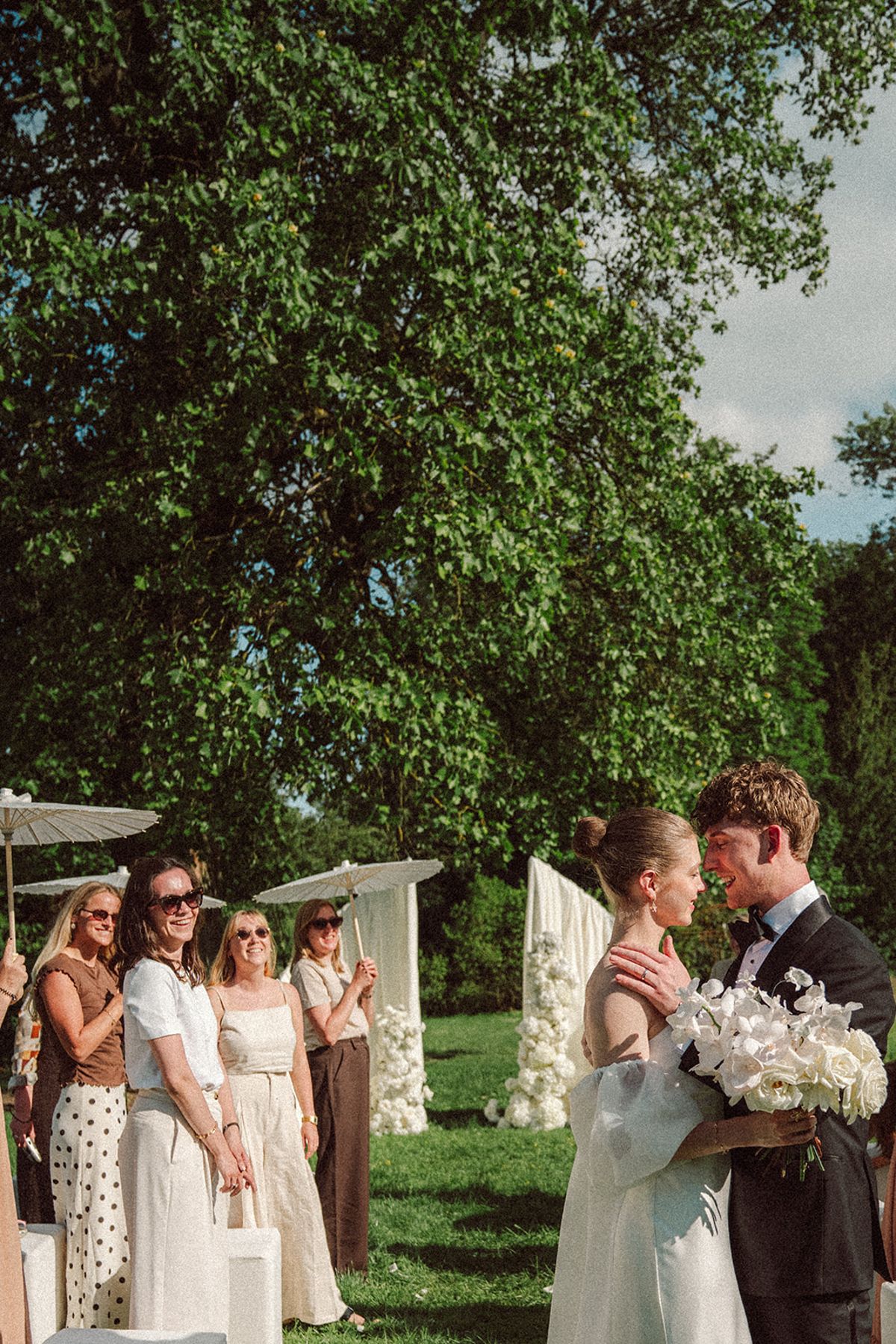 Guests holding parasols watching the ceremony, couple in the background