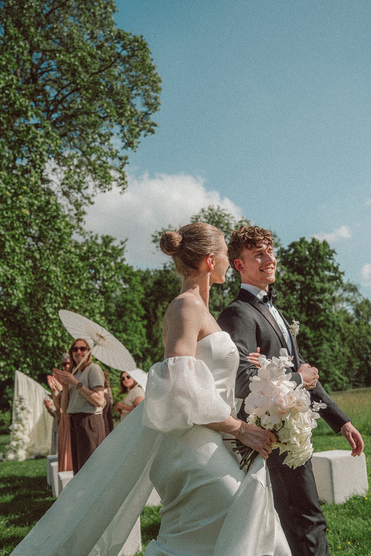 Bride and groom walking past guests holding parasols