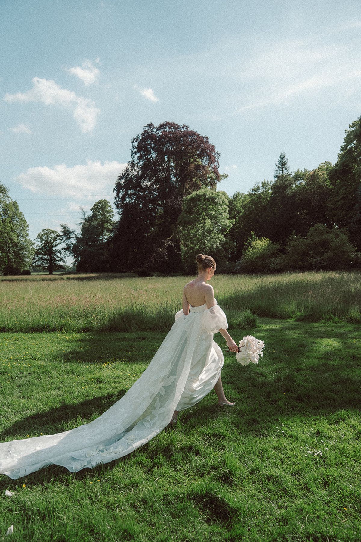 Bride walking alone through a field, seen from behind