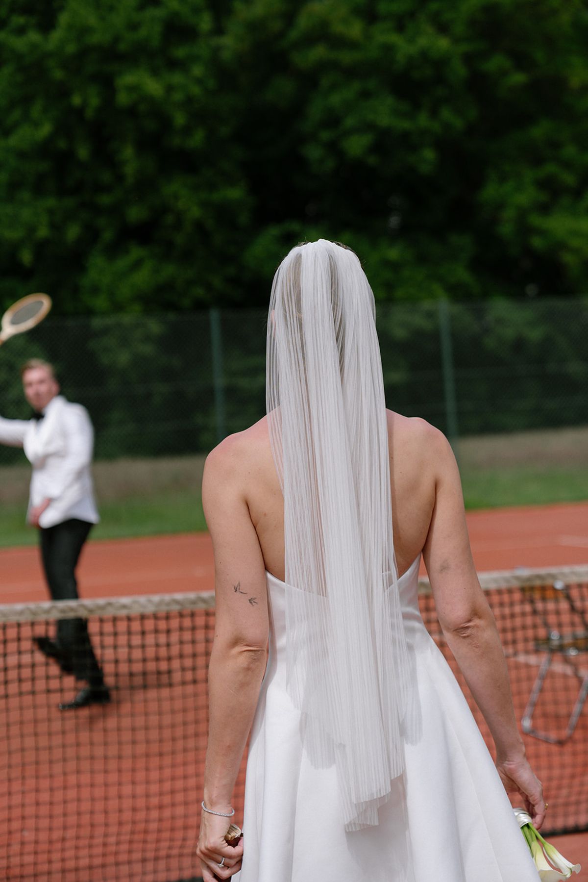 Bride from behind in a veil, walking onto the tennis court