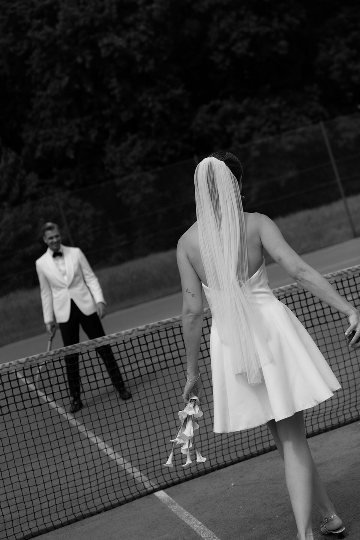 Bride and groom at the tennis net, bride facing away, black and white