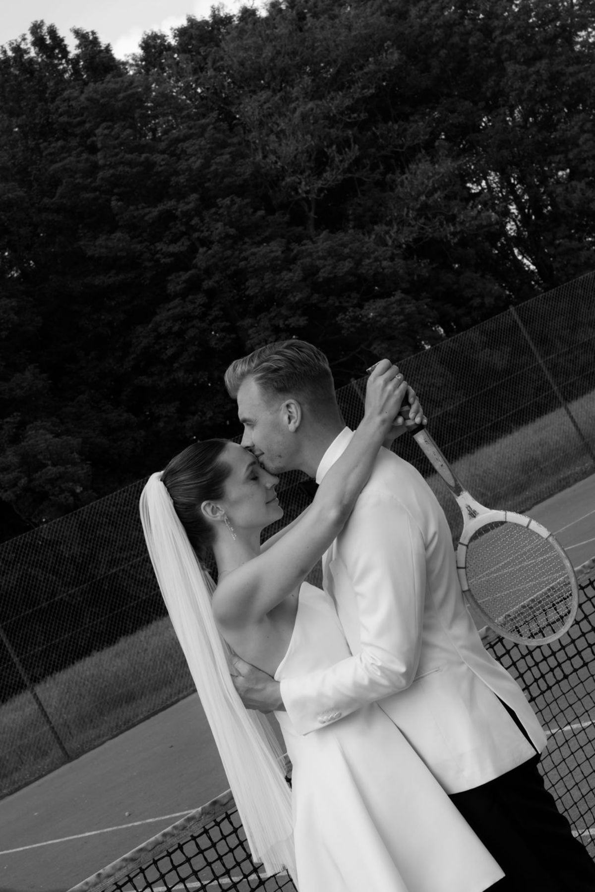 Bride and groom in a close embrace with a tennis racket, black and white