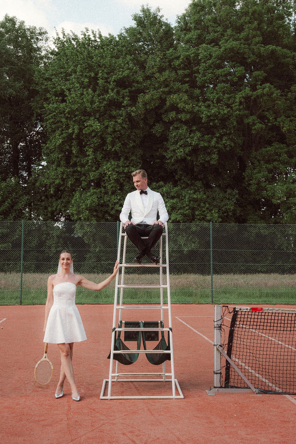 Bride standing on the umpire's chair, groom looking up at her