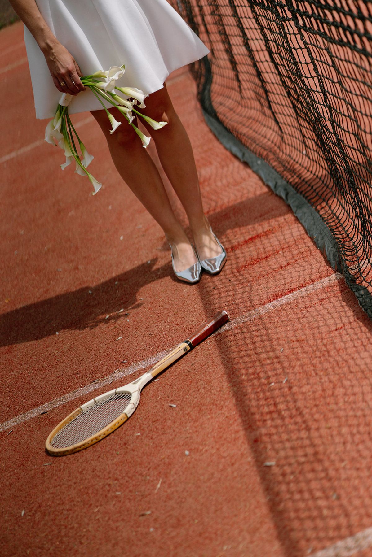 Detail of the bride's shoes and a tennis racket on the court