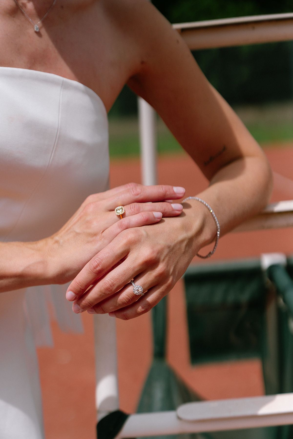 Bride and groom's hands together, showing the wedding rings, on the tennis court