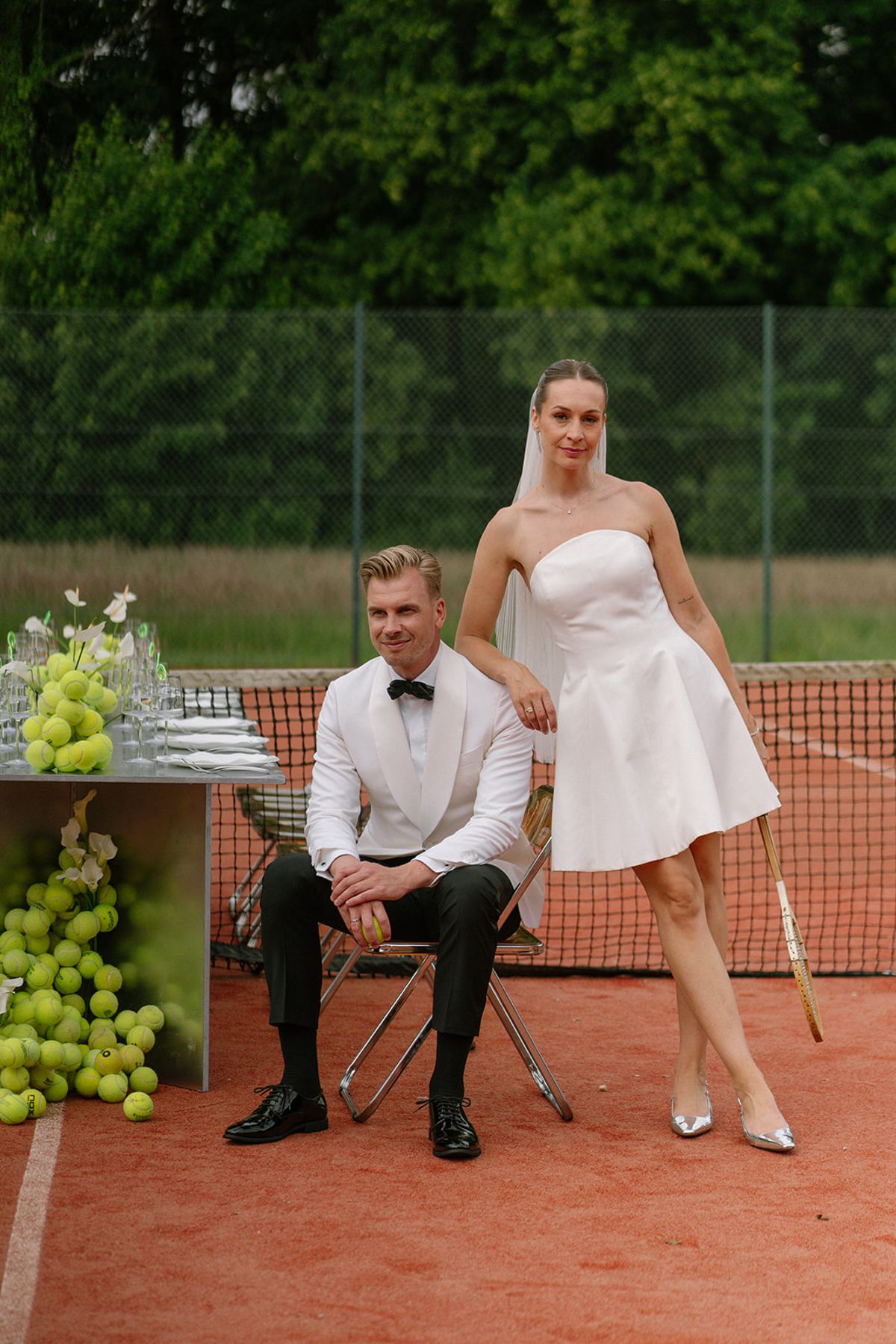 Bride and groom standing together on the tennis court in editorial dress