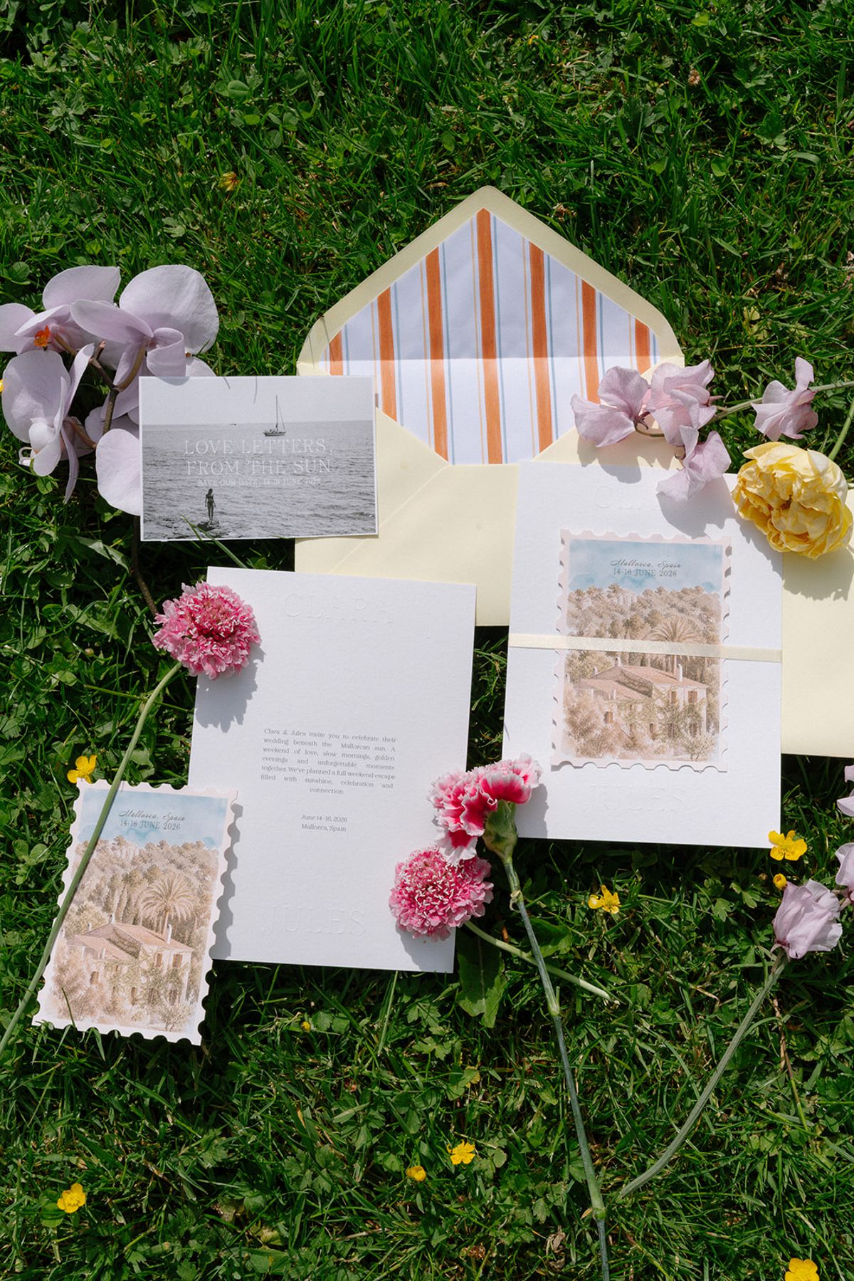 Wedding stationery flat lay on grass with dahlias and orchid stems