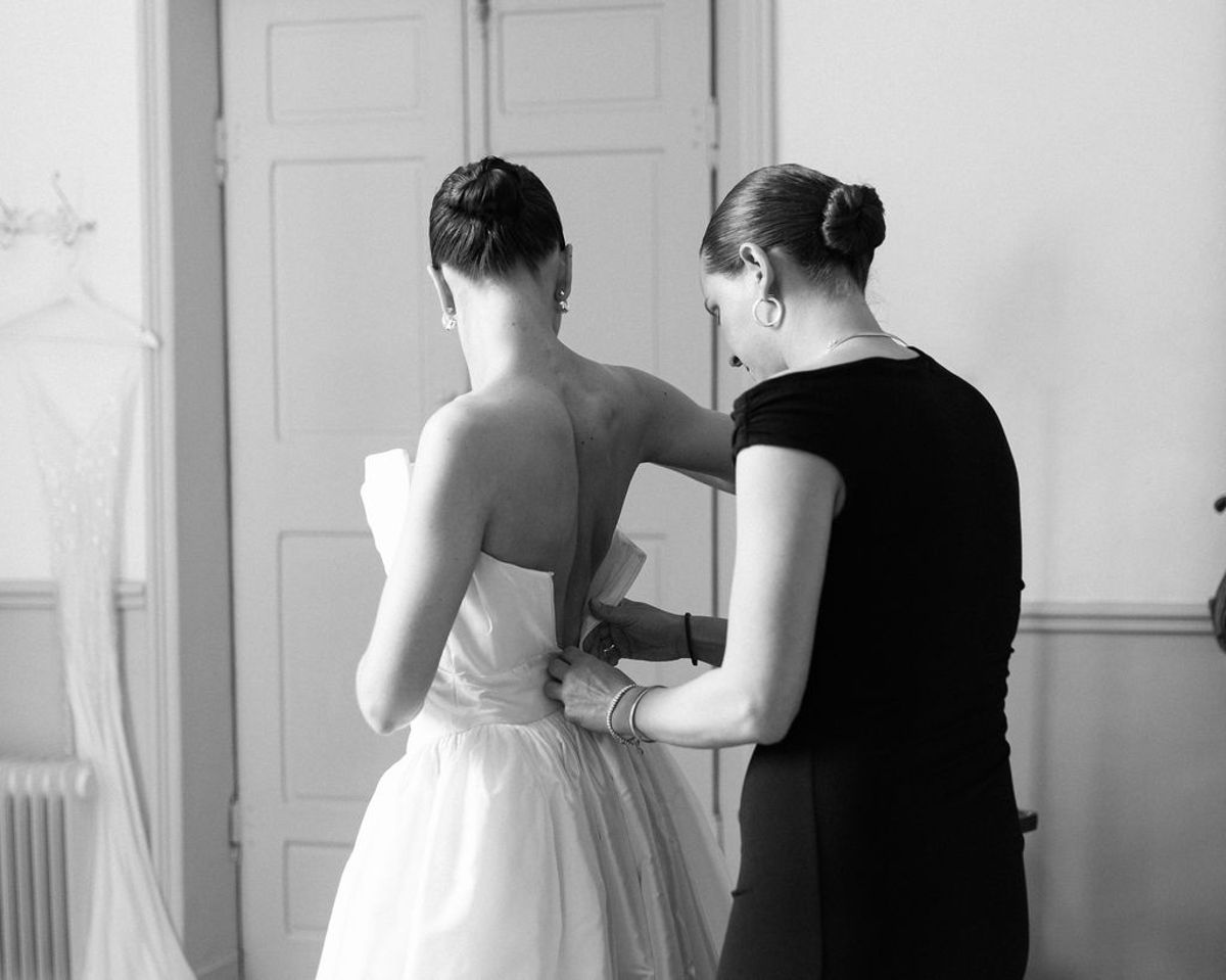 An attendant fastens the back of Clara's wedding dress