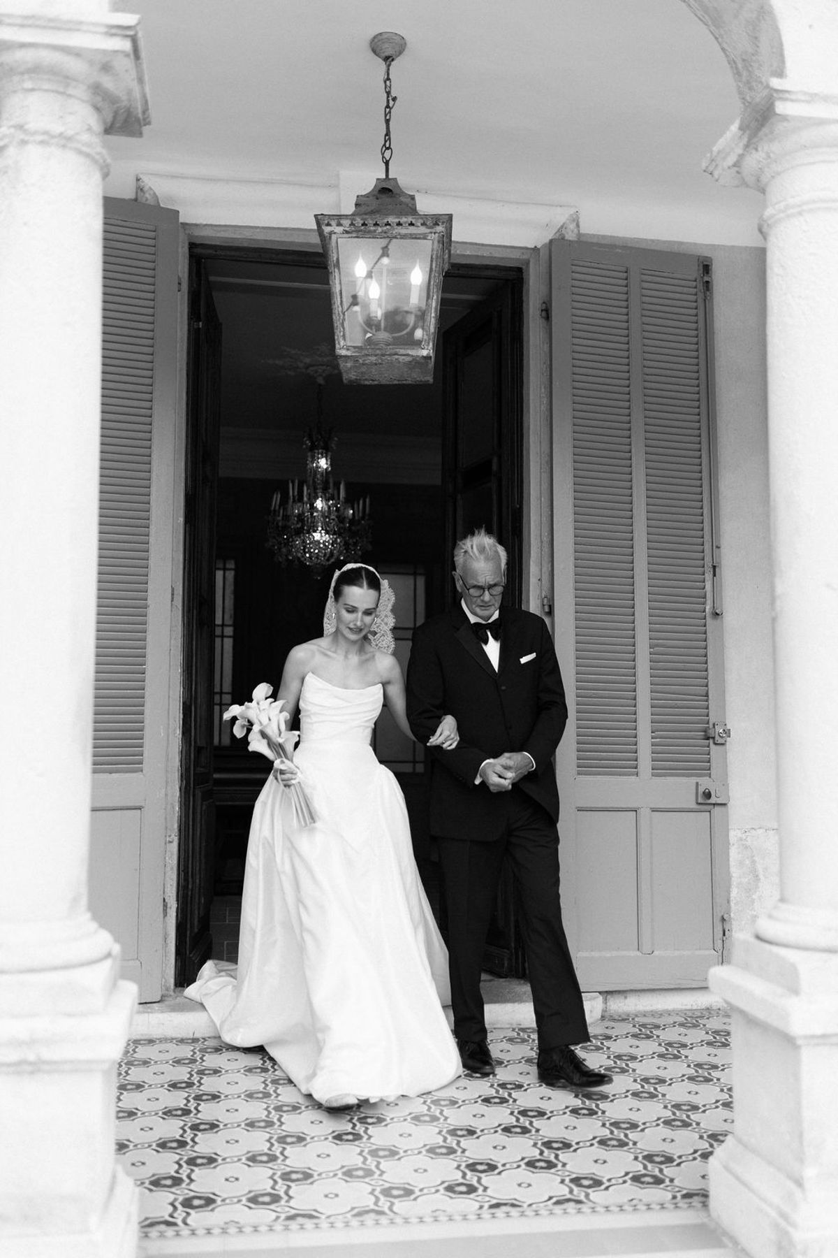 Clara descends the stairs on her father's arm, captured in black and white
