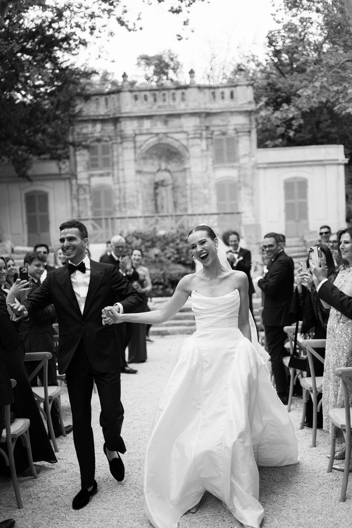 Clara and Constantin walk together as guests applaud, captured in black and white