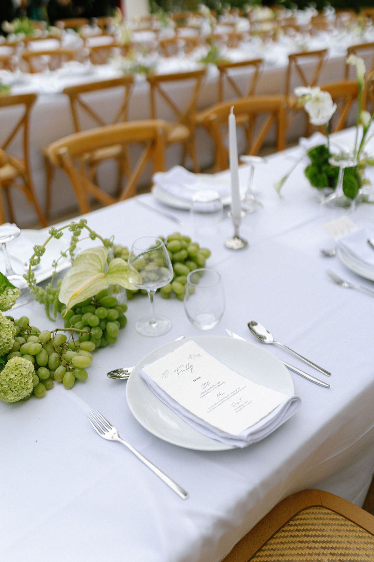 A place setting with grapes and glassware on white linen