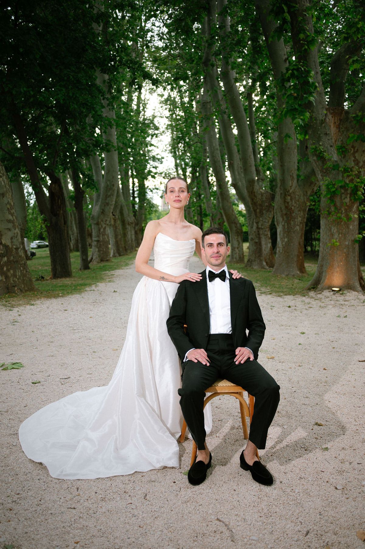 Clara sits on Constantin's lap on a tree-lined path in the park at Bastide de Toursainte