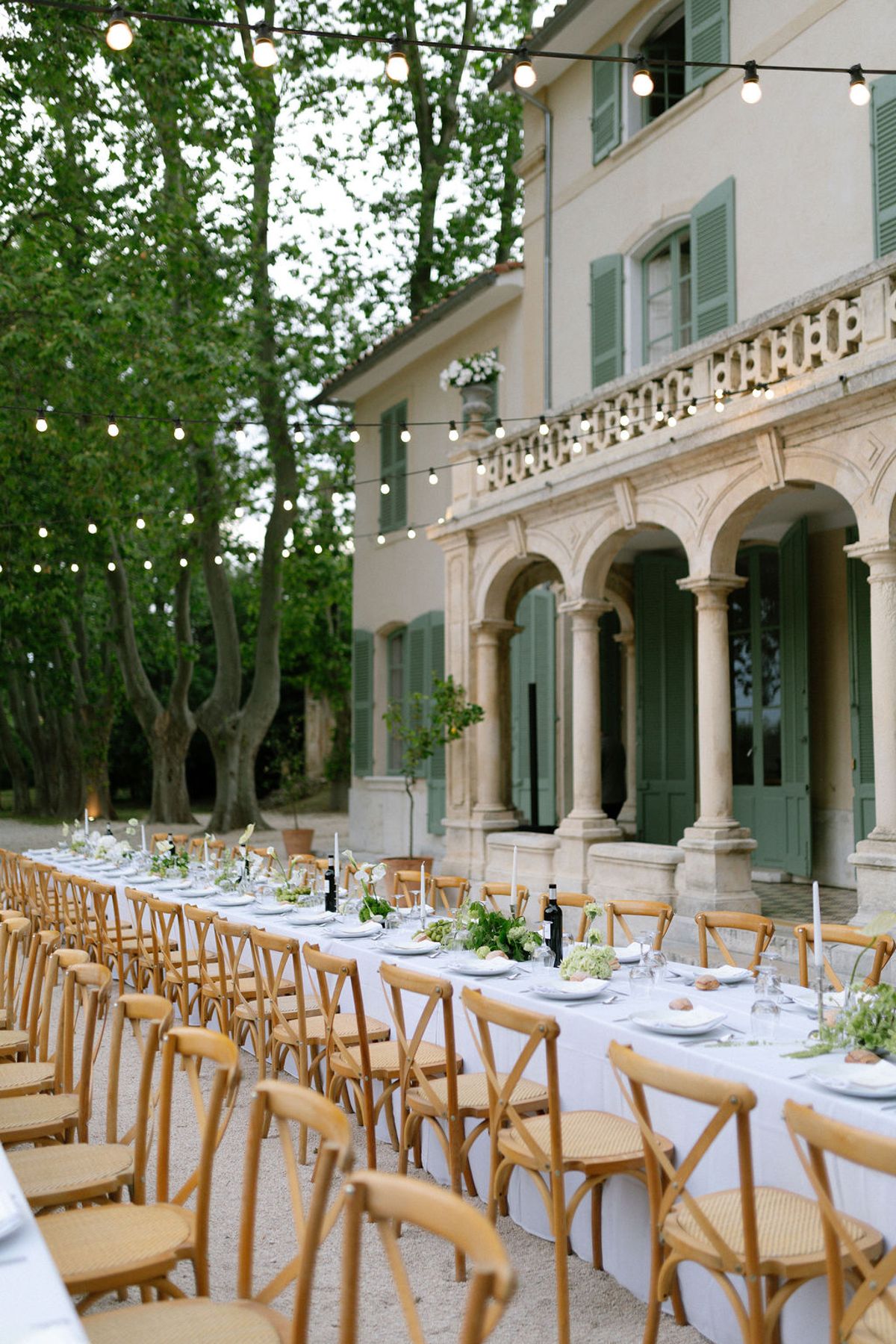 A long dinner table set outdoors in front of Bastide de Toursainte