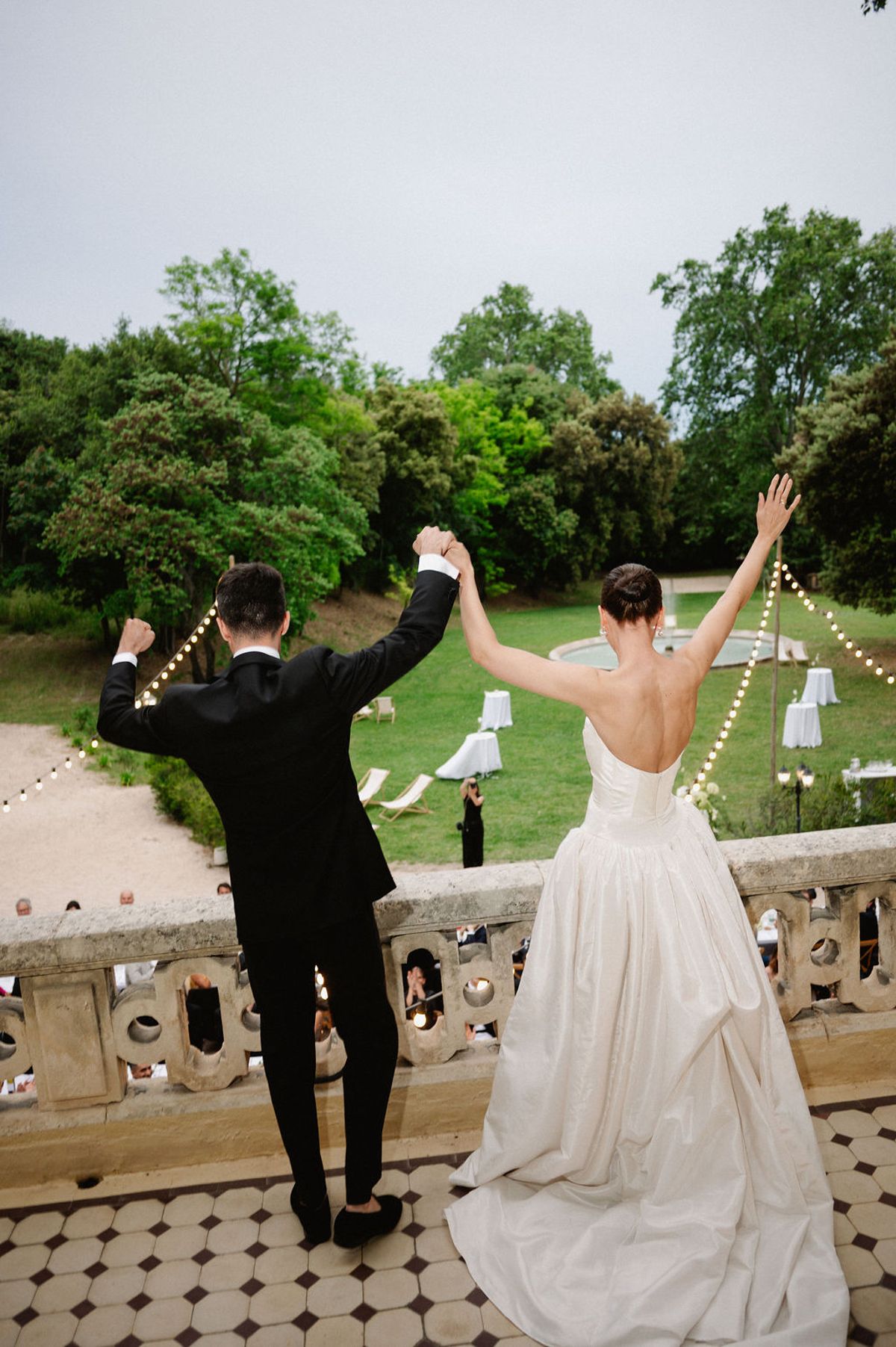 Clara and Constantin dance with arms raised on the terrace as string lights are strung overhead