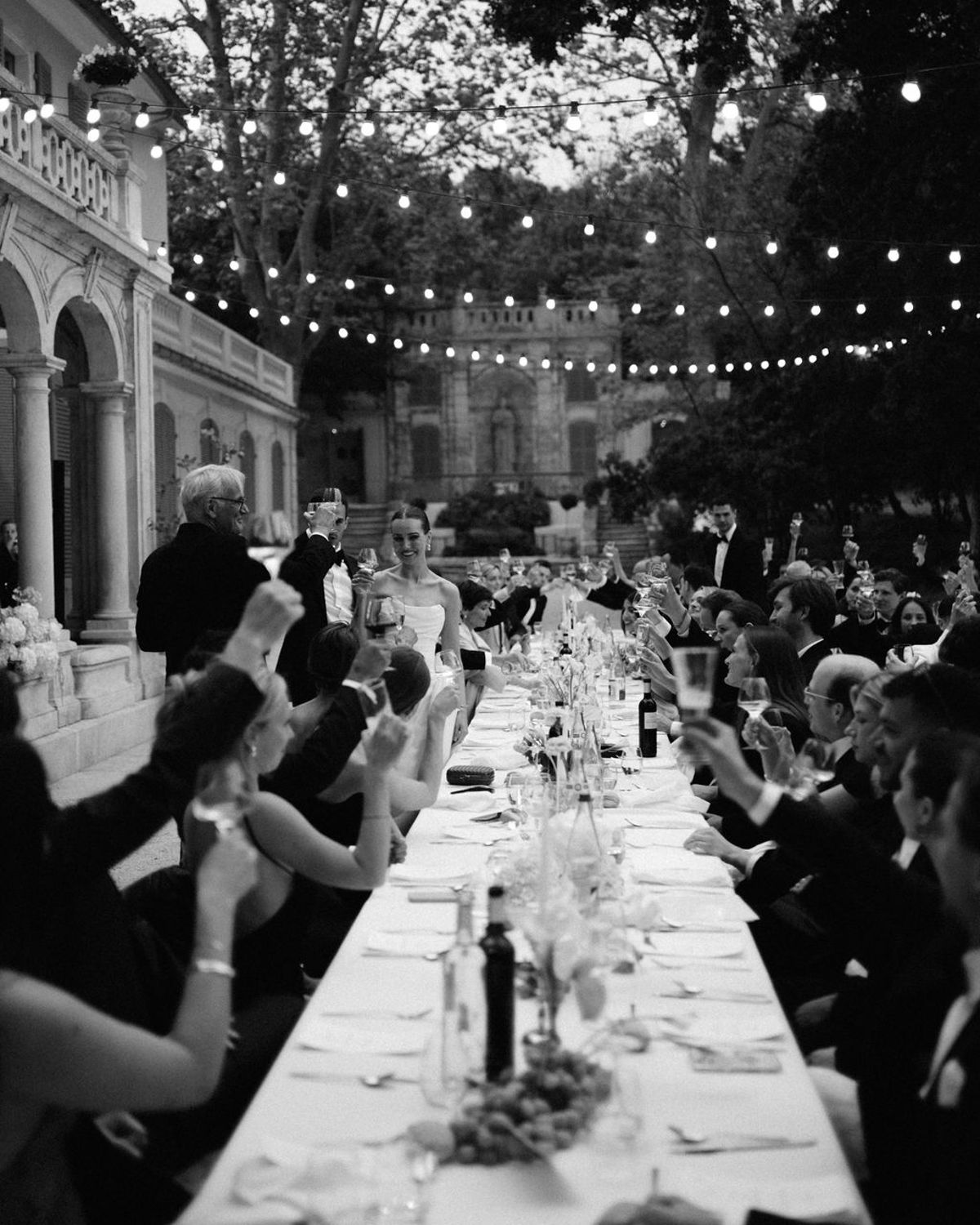 Guests applaud around the long dinner table, captured in black and white