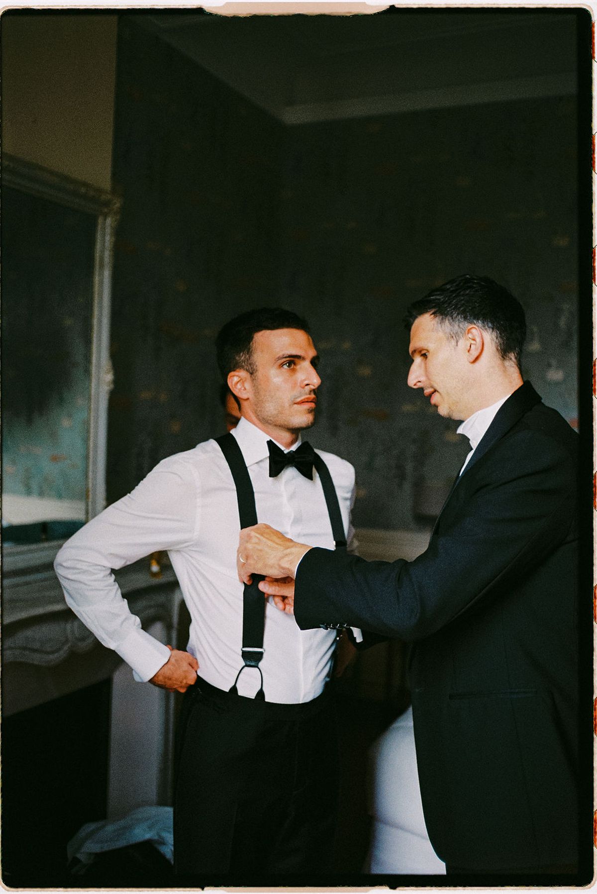 Two groomsmen adjust their suspenders while getting ready